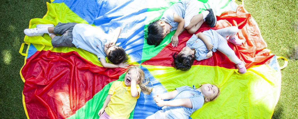 Kindergarten children lying on colourful circle on grass